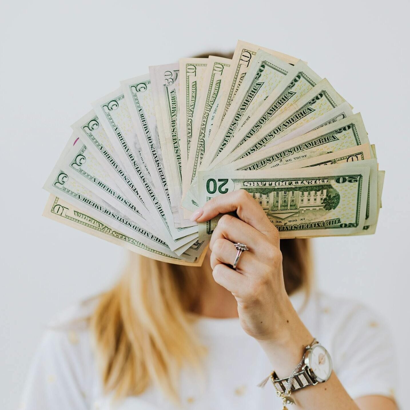 Woman holding a fan of US dollar bills in front of her face.